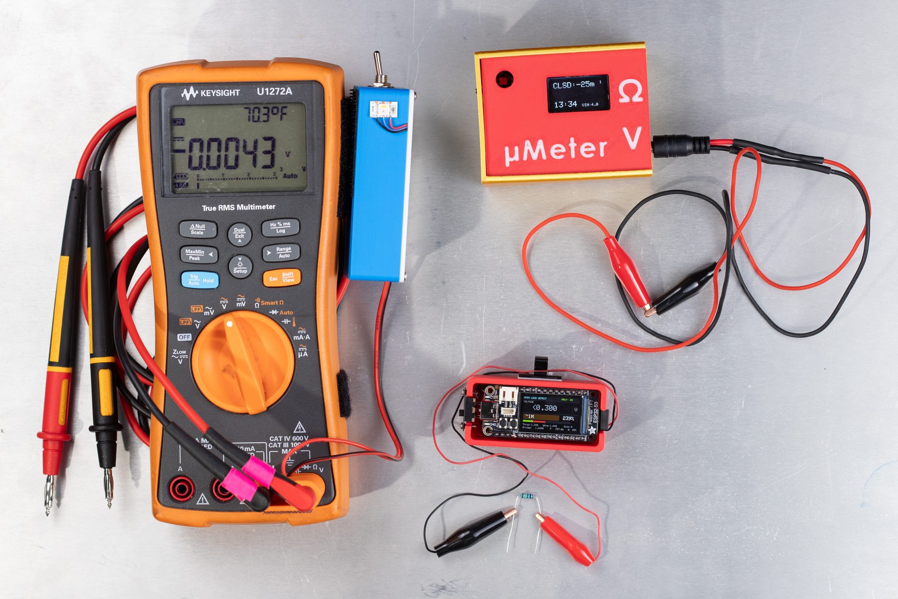 The family of devices: a parallel detector clipped onto a Keysight DMM, a red standalone unit, and a compact MCU build.